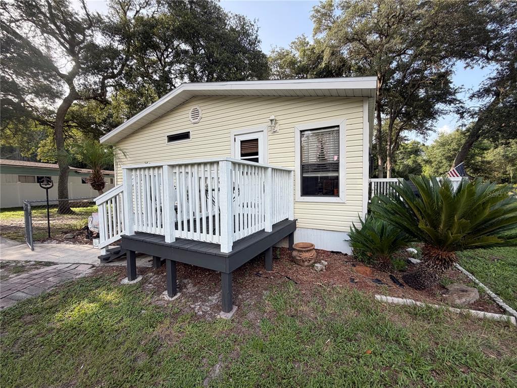 A light yellow mobile home features a dark gray deck with white railings and landscaping — 40235 OVERLOOK DRIVE, EUSTIS, FL