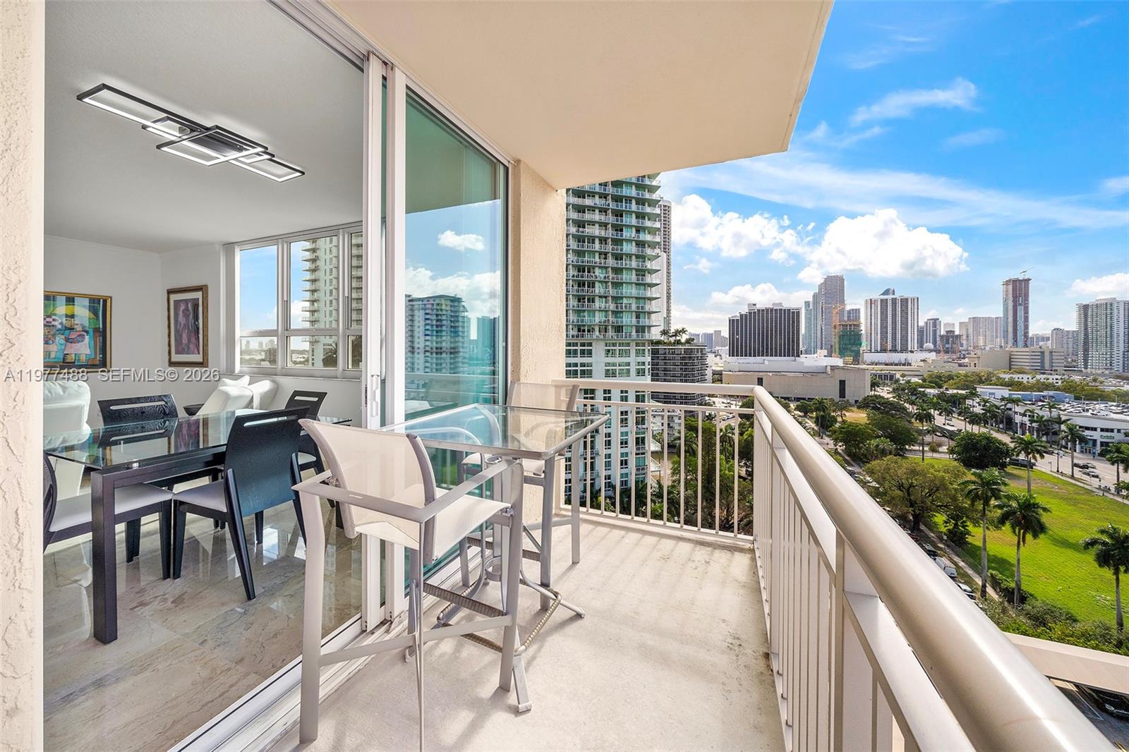 A balcony with a glass table and chairs overlooks a city skyline and green space — 2000 N Bayshore Dr # 1502, Miami FL 33137, MIAMI, FL