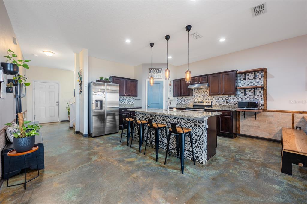 A kitchen features dark wood cabinets, a patterned island with bar stools, and concrete flooring — 16434 WINDING BLOSSOM DRIVE, GROVELAND, FL