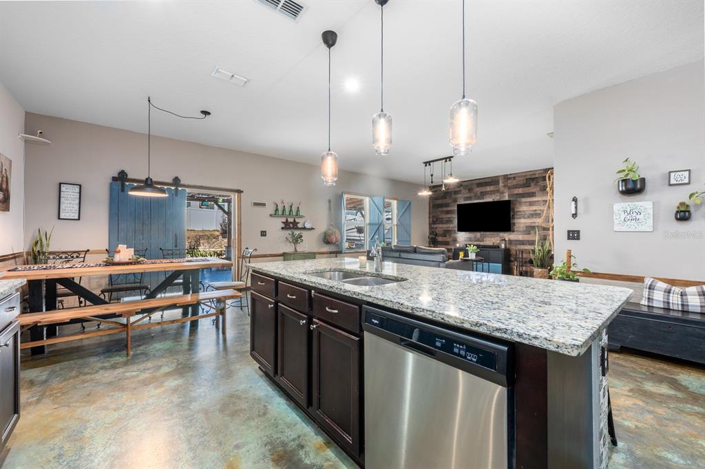 A kitchen island with a granite countertop and stainless steel dishwasher faces a dining area — 16434 WINDING BLOSSOM DRIVE, GROVELAND, FL
