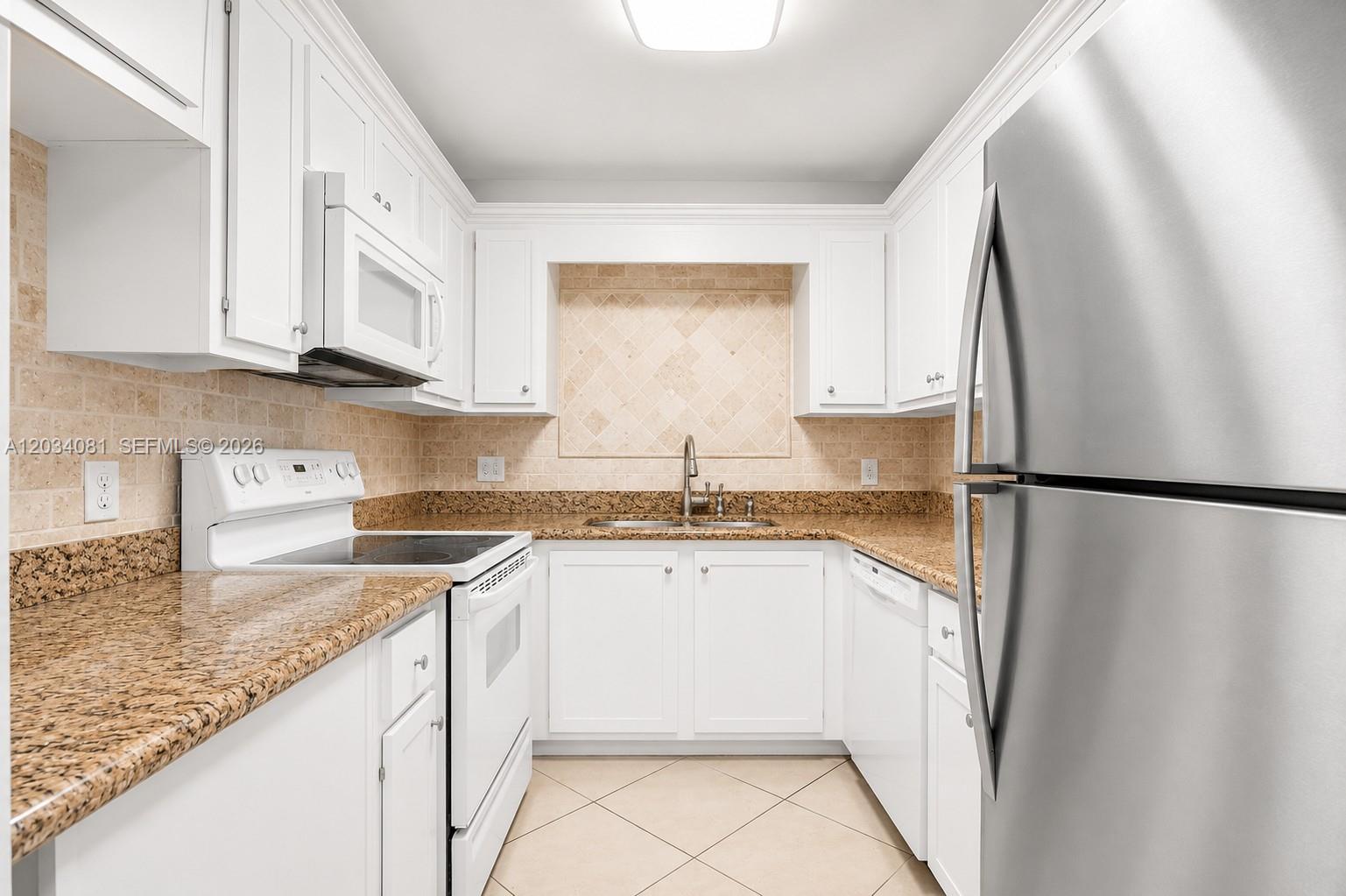A kitchen features white cabinets, granite countertops, stainless steel appliances, and a tiled backsplash — 5961 N Falls Cir Dr # 309, Lauderhill FL 33319, LAUDERHILL, FL