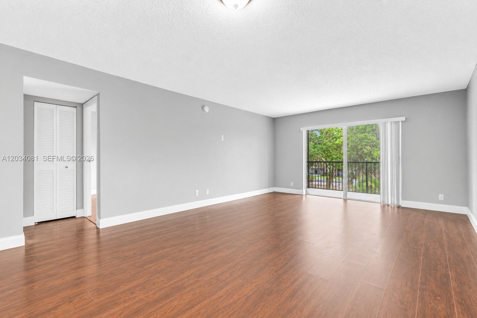 An empty living room features gray walls, wood-look flooring, and a sliding glass balcony door — 5961 N Falls Cir Dr # 309, Lauderhill FL 33319, LAUDERHILL, FL