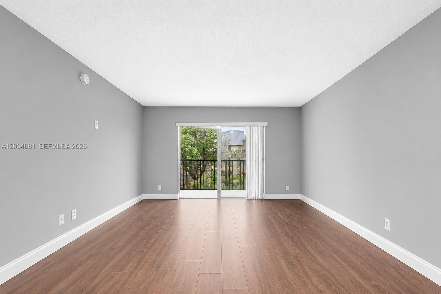 An empty room with gray walls, wood-look flooring, and a sliding glass door to a balcony — 5961 N Falls Cir Dr # 309, Lauderhill FL 33319, LAUDERHILL, FL