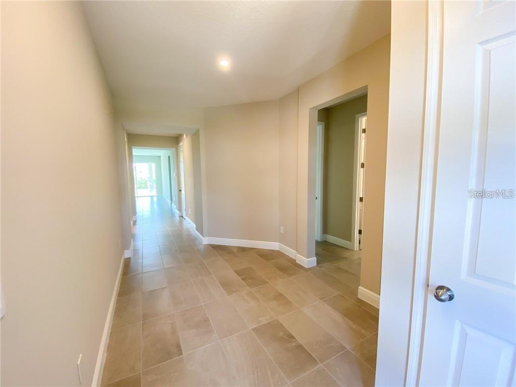 A hallway with light-colored tile flooring leads toward a bright doorway in the distance — 16125 PARKWYN STREET, WINTER GARDEN, FL
