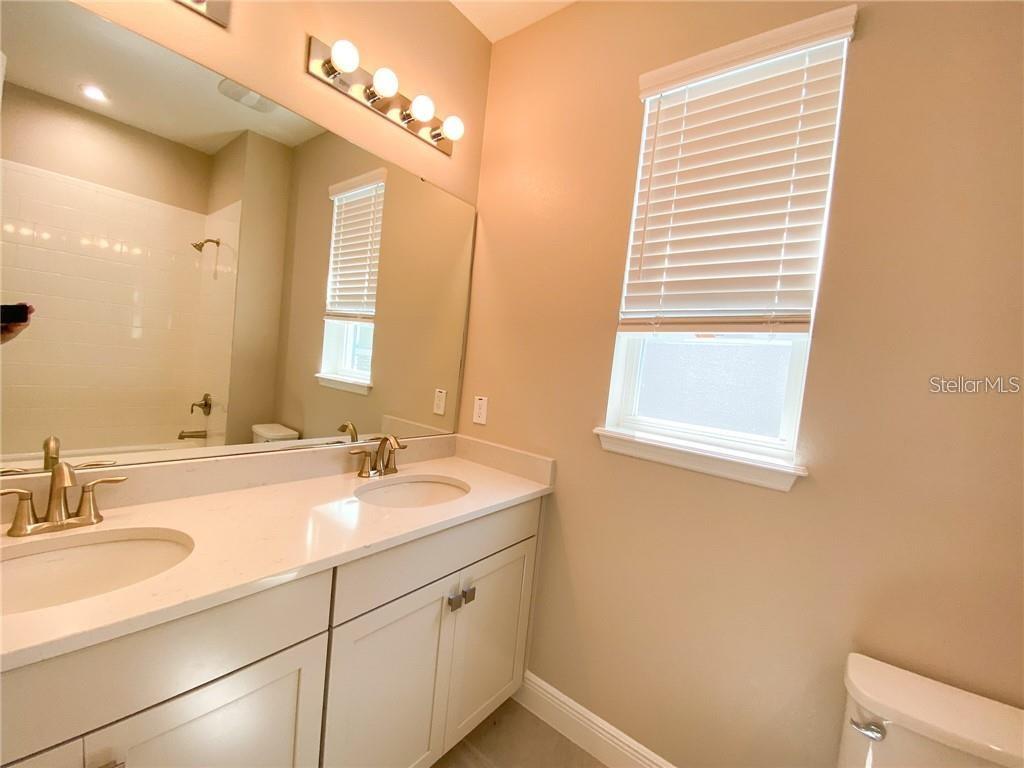 A bathroom features a double vanity with white cabinets, gold fixtures, and a large mirror — 16125 PARKWYN STREET, WINTER GARDEN, FL