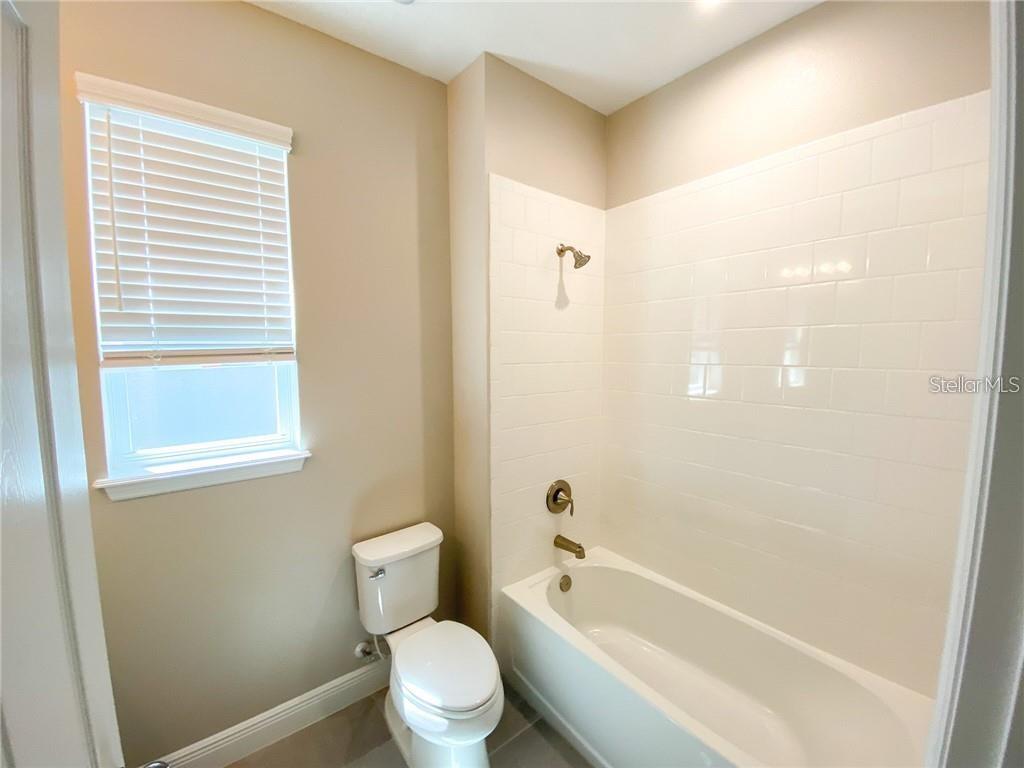 A bathroom features a white bathtub with subway tile walls, a toilet, and a window — 16125 PARKWYN STREET, WINTER GARDEN, FL