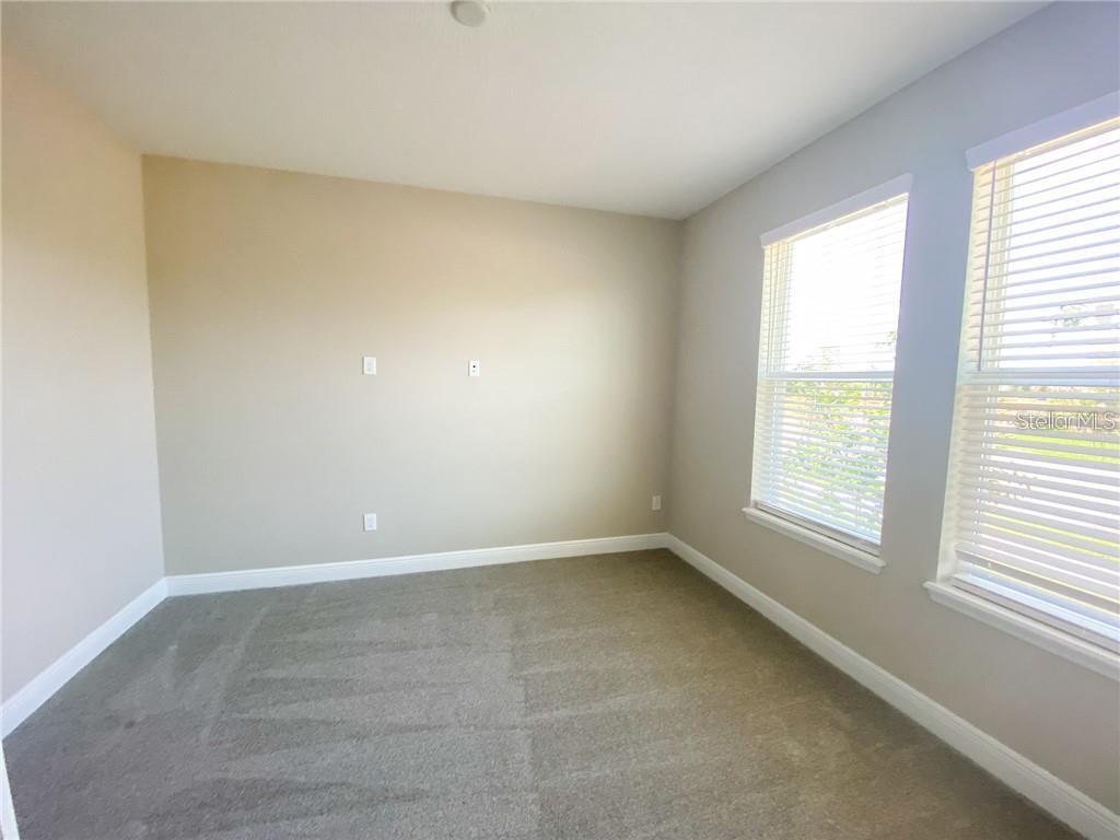 An empty bedroom features beige walls, gray carpeting, and two windows with white blinds — 16125 PARKWYN STREET, WINTER GARDEN, FL