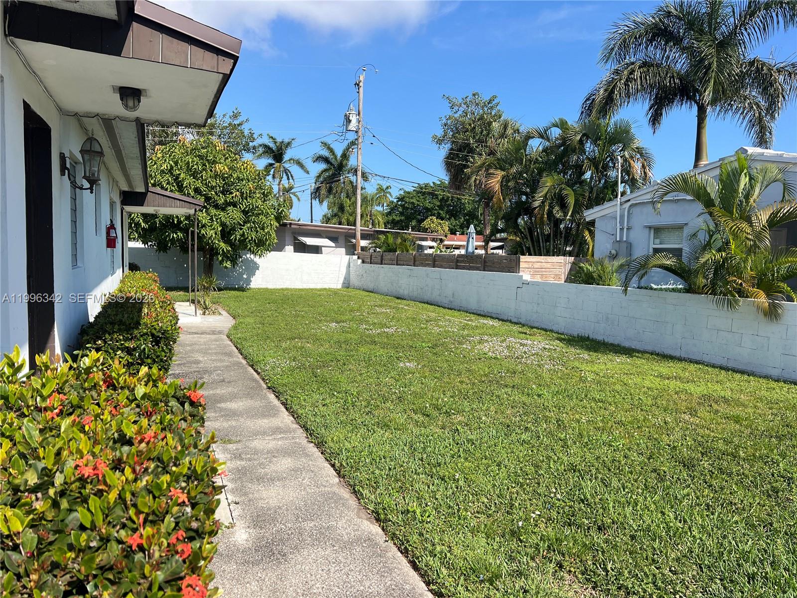 A concrete walkway runs alongside a house exterior next to a grassy backyard and wall — 809 NE 2nd St # 2, Hallandale Beach FL 33009, HALLANDALE BEACH, FL