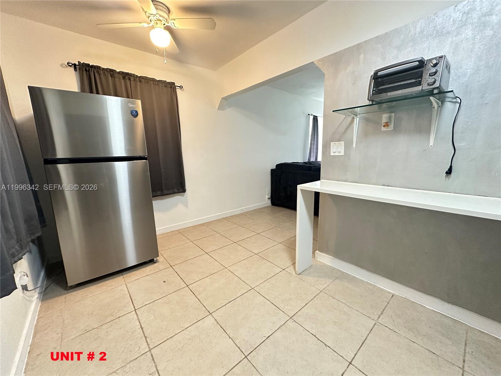 A kitchen area features a stainless steel refrigerator, tile flooring, and a wall-mounted shelf — 809 NE 2nd St # 2, Hallandale Beach FL 33009, HALLANDALE BEACH, FL