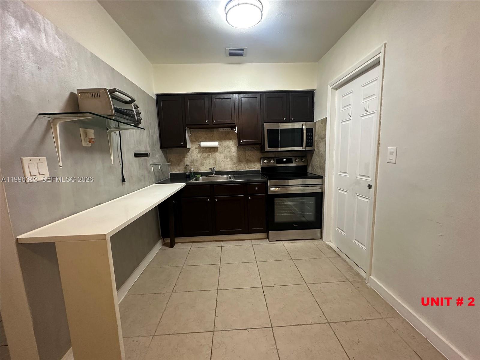 A kitchen features dark wood cabinets, stainless steel appliances, and a white breakfast bar — 809 NE 2nd St # 2, Hallandale Beach FL 33009, HALLANDALE BEACH, FL
