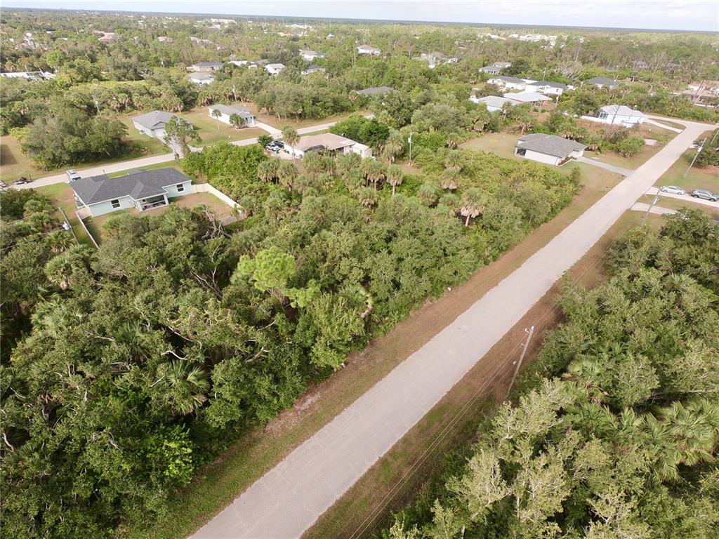 An aerial view shows a vacant, wooded lot situated between residential houses and a paved road — 7145 FELICIA STREET, PORT CHARLOTTE, FL
