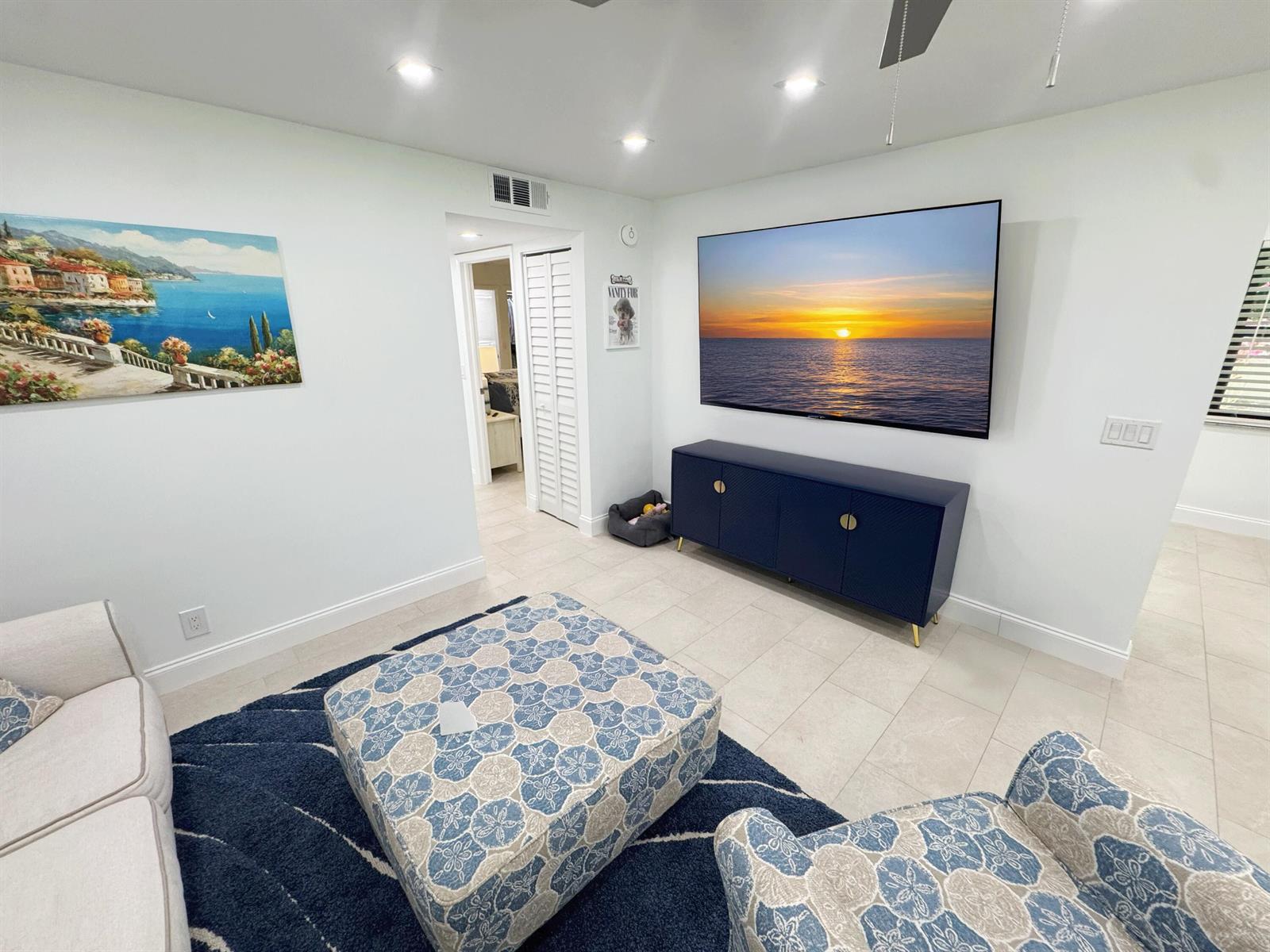 A living room features a wall-mounted television, a blue media console, and patterned furniture — 18 Piedmont A, Delray Beach FL 33484, DELRAY BEACH, FL