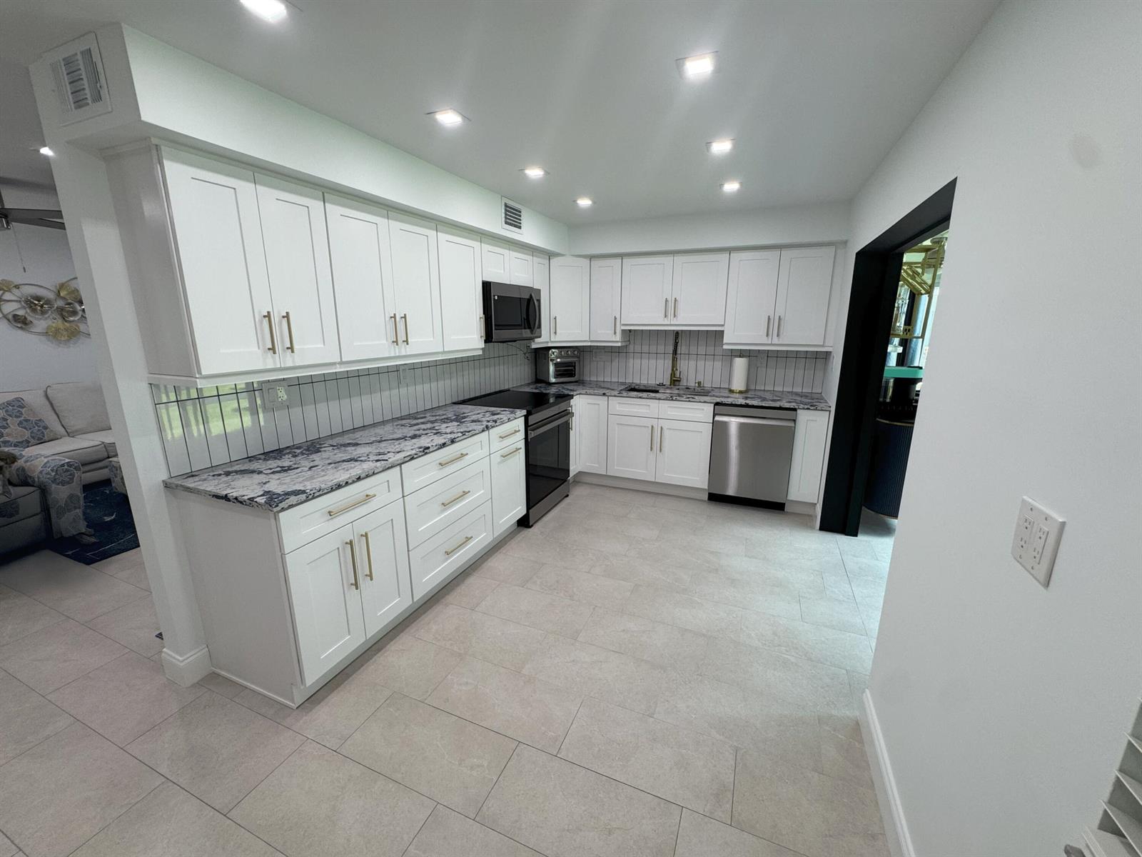 A kitchen features white cabinets, dark granite countertops, stainless steel appliances, and light tile flooring — 18 Piedmont A, Delray Beach FL 33484, DELRAY BEACH, FL