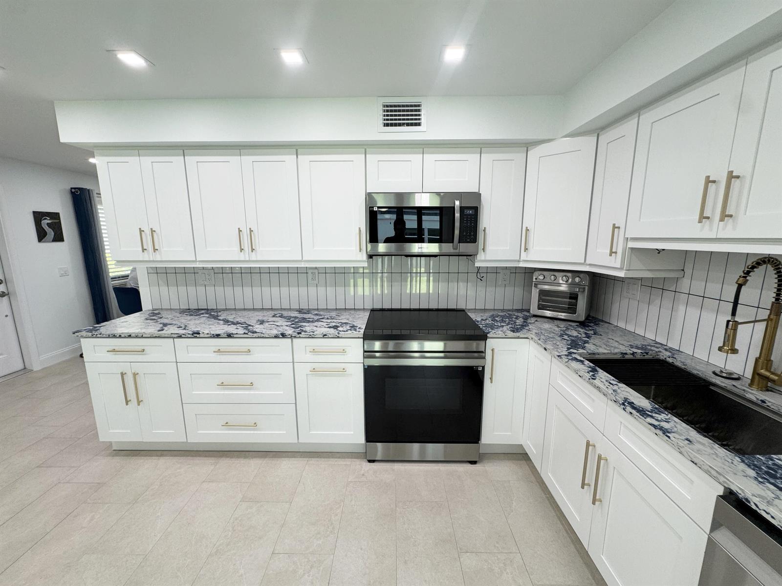 A kitchen features white cabinets, blue-veined granite countertops, stainless steel appliances, and vertical tile backsplash — 18 Piedmont A, Delray Beach FL 33484, DELRAY BEACH, FL