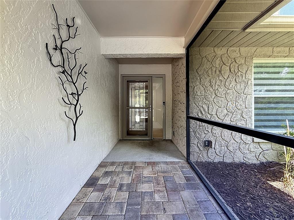 A covered entryway features a paver floor, a decorative metal wall sculpture, and a screen — 2632 CAMILLE DRIVE, PALM HARBOR, FL
