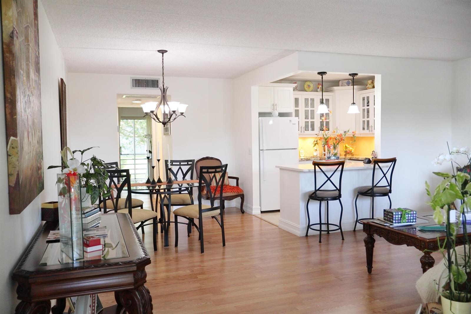 A dining area and kitchen with white cabinets, a breakfast bar, and wood-look flooring — 3400 Springdale Boulevard # 214, Palm Springs FL 33461, PALM SPRINGS, FL