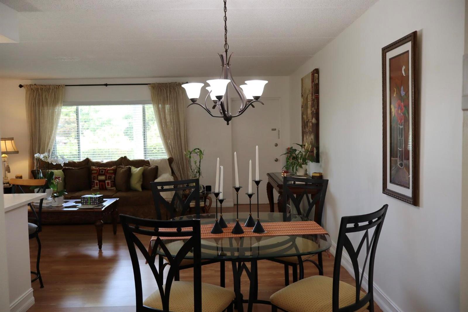 A dining area with a glass table and chandelier opens into a living room — 3400 Springdale Boulevard # 214, Palm Springs FL 33461, PALM SPRINGS, FL
