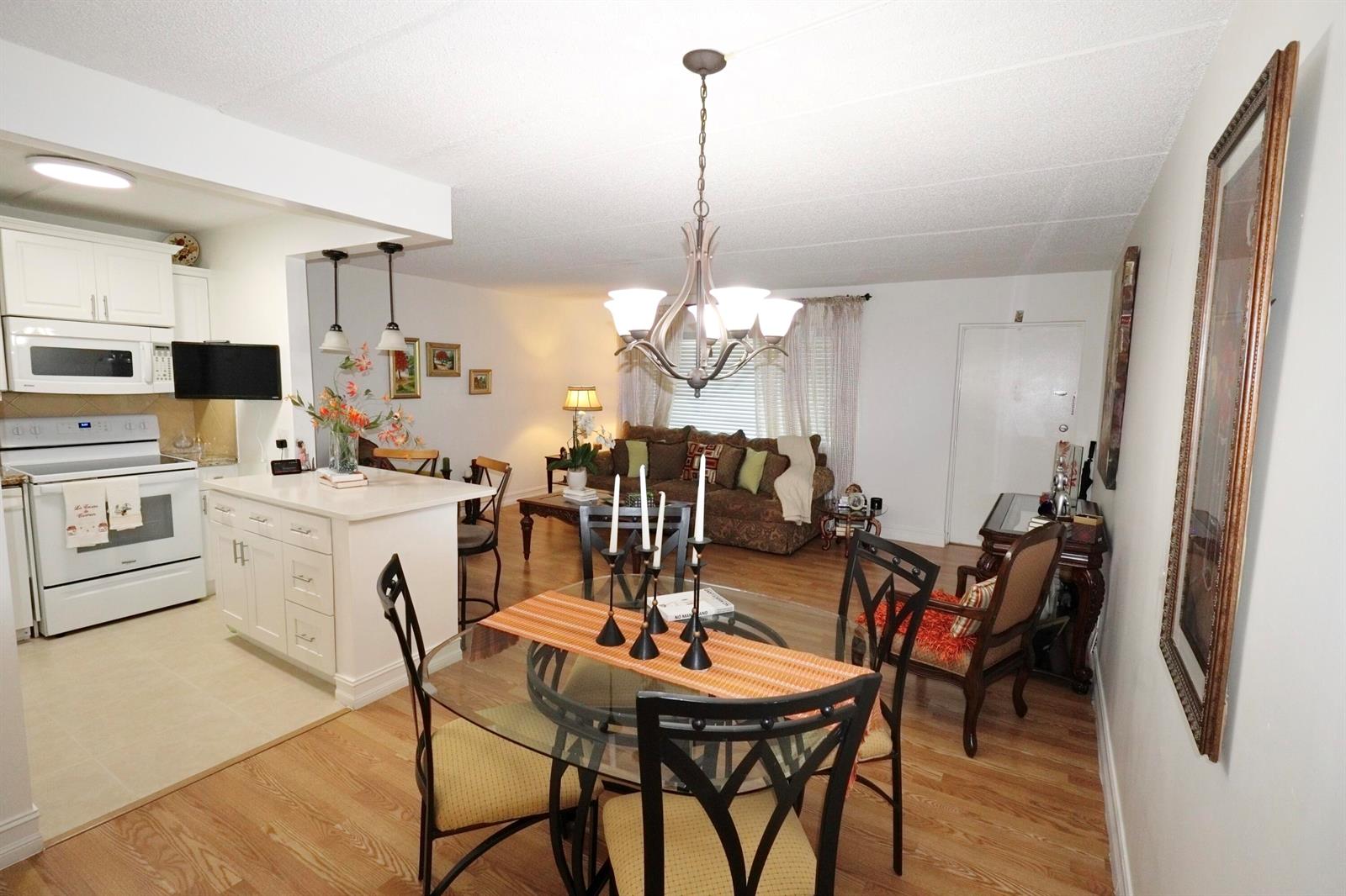 An open-concept living and dining area features a kitchen with white cabinets and wood flooring — 3400 Springdale Boulevard # 214, Palm Springs FL 33461, PALM SPRINGS, FL