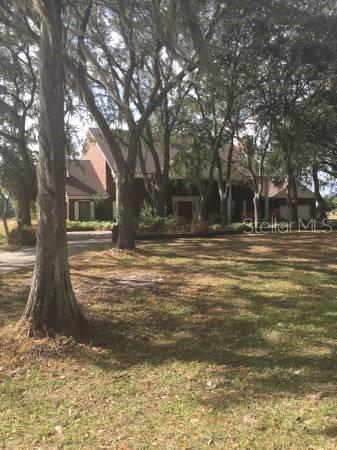 A two-story brick house sits behind large trees on a grassy lot — 12537 TOMAR DRIVE, THONOTOSASSA, FL