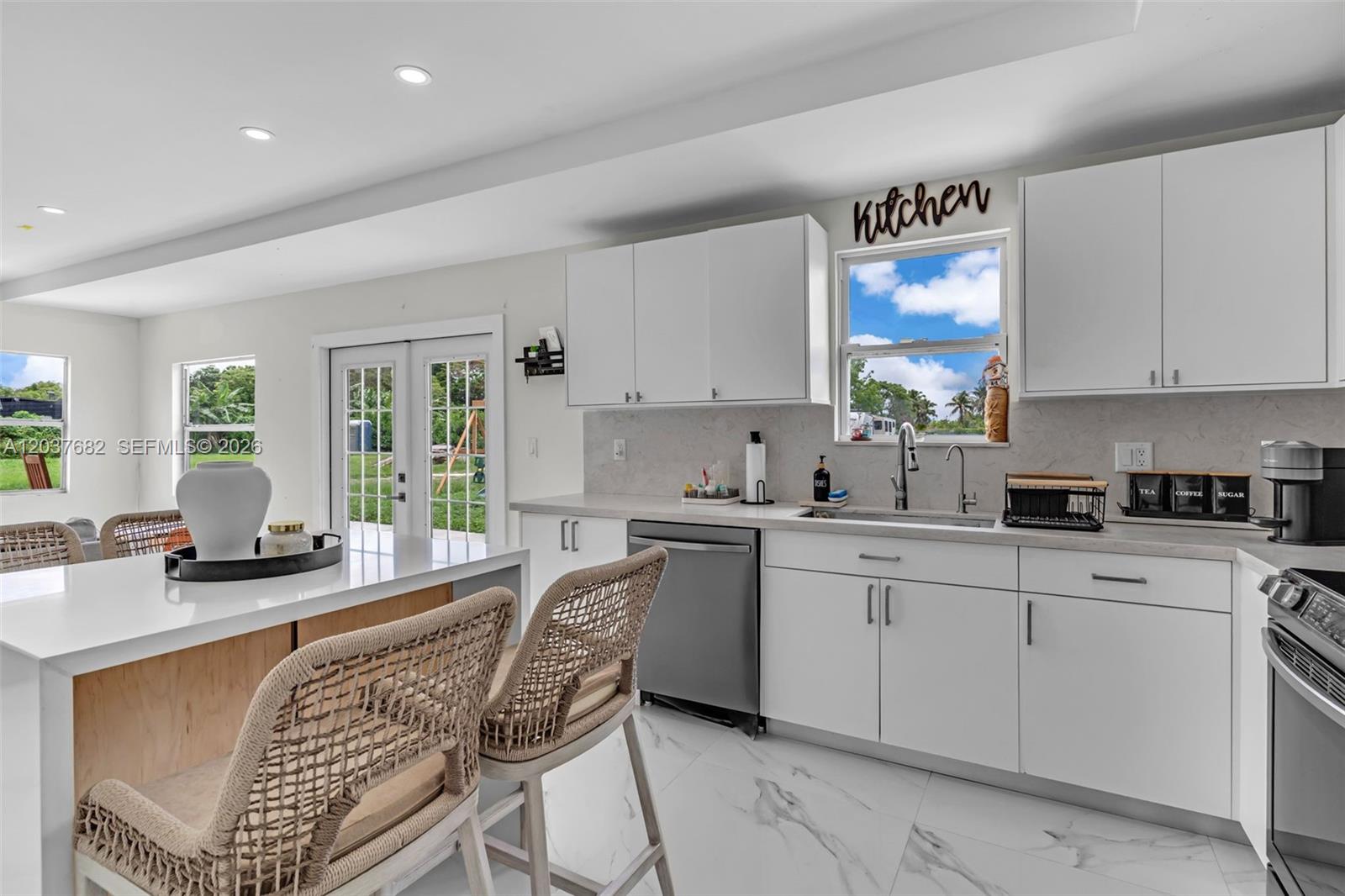 A modern kitchen features white cabinetry, a marble-topped island with woven chairs, and stainless appliances — 20304 SW 186th St, Miami FL 33187, MIAMI, FL
