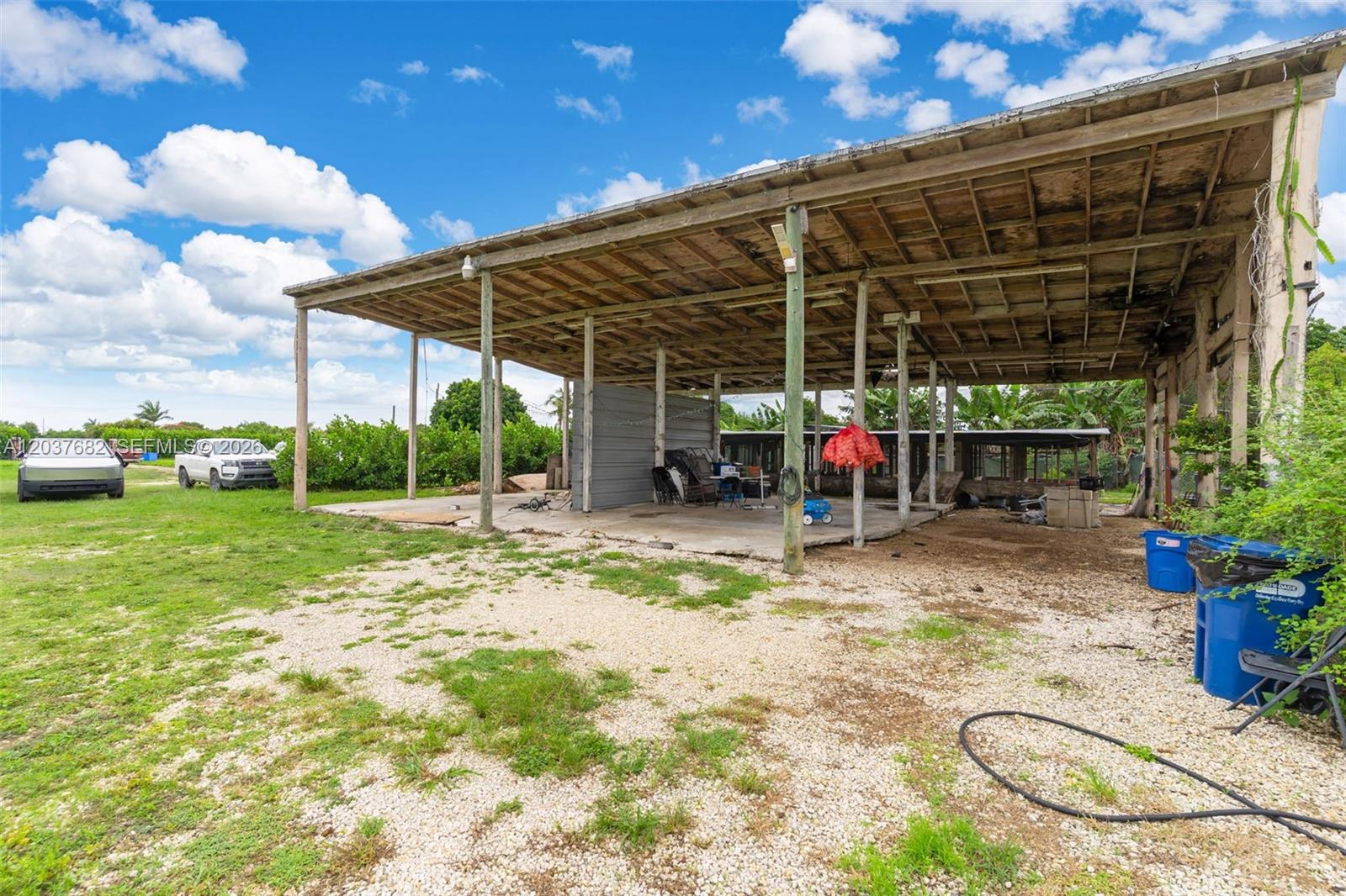 An open-sided wooden pole barn structure sits on a gravel lot under a blue sky — 20304 SW 186th St, Miami FL 33187, MIAMI, FL