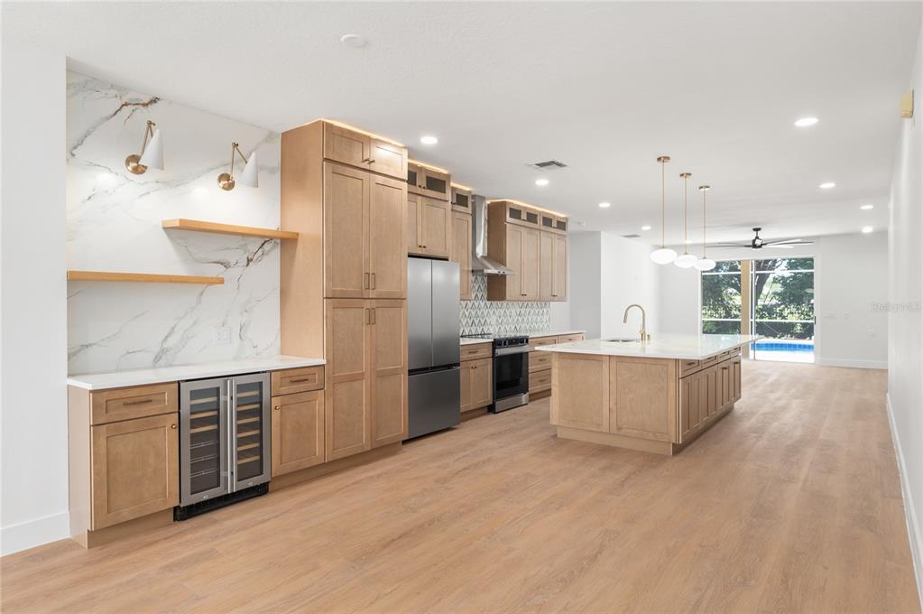 A modern kitchen features light wood cabinetry, marble-look backsplash, stainless steel appliances, and a large island — 2424 STONE CROSS CIRCLE, ORLANDO, FL