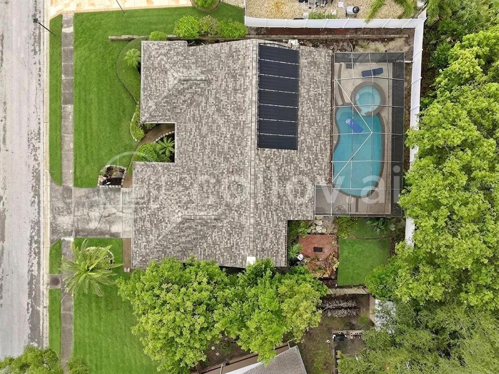 An aerial view shows a house with a shingled roof, solar panels, and a screened pool — 1071 PERSIMMON DRIVE, PALM HARBOR, FL