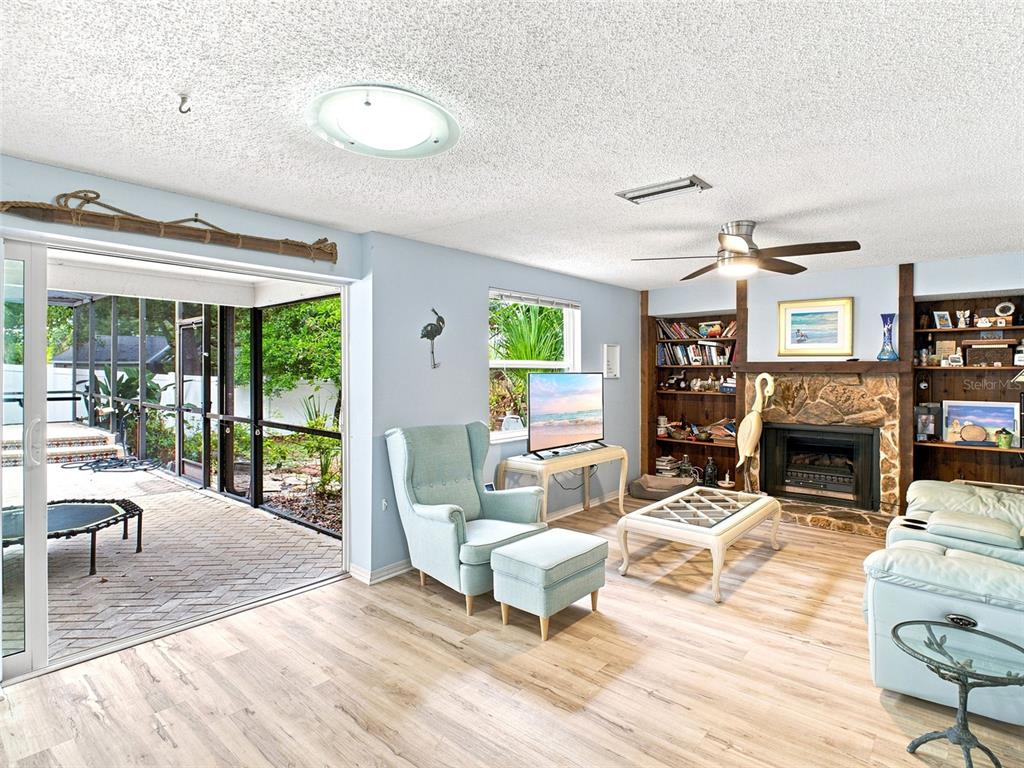 A living room features light wood flooring, a stone fireplace, built-in shelves, and a sliding door — 1071 PERSIMMON DRIVE, PALM HARBOR, FL