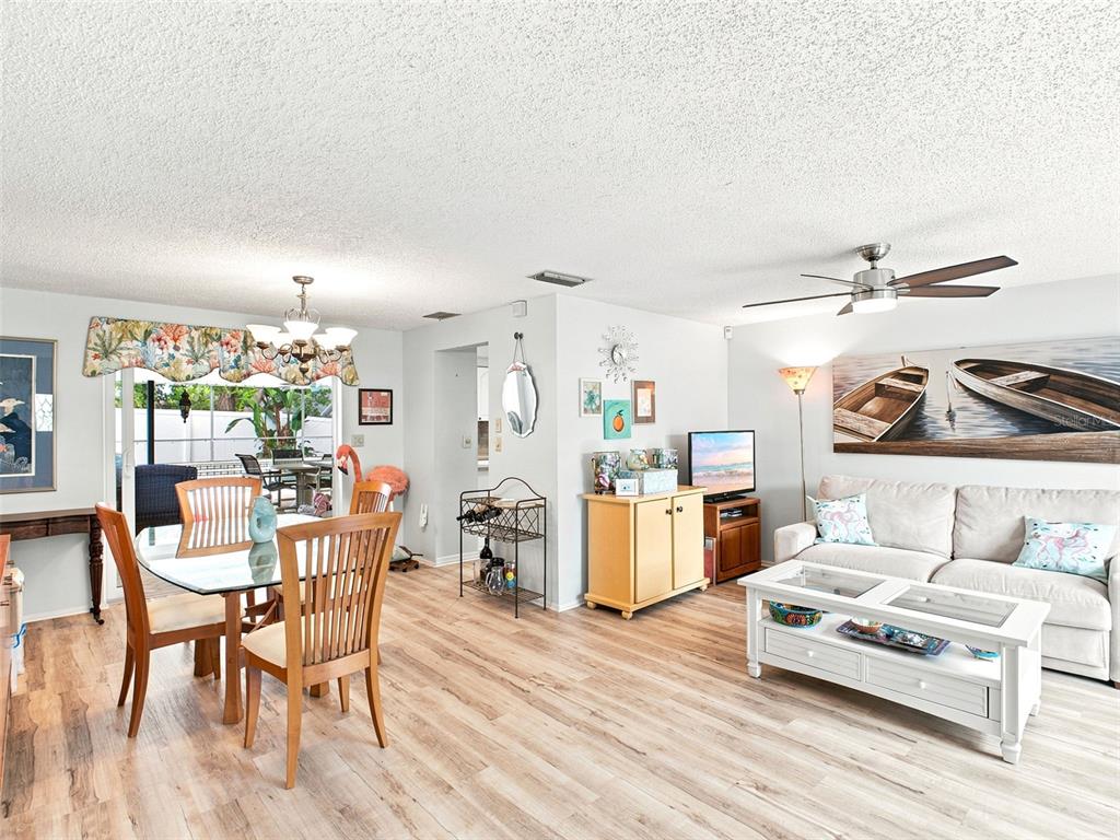 A living and dining area features light wood-look flooring, a ceiling fan, and sliding glass doors — 1071 PERSIMMON DRIVE, PALM HARBOR, FL
