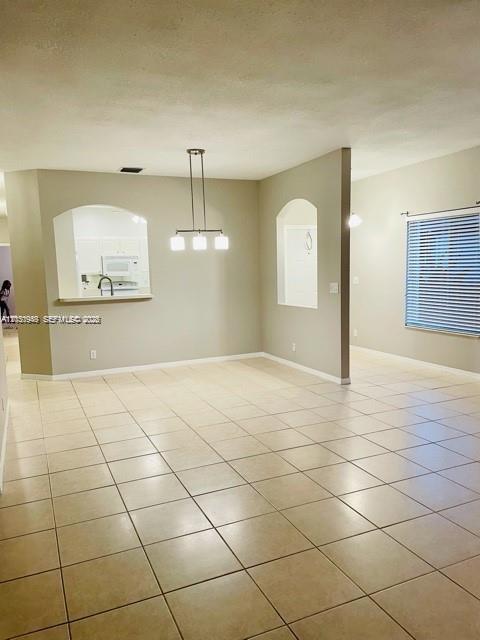 A dining area features beige tile flooring, a modern pendant light, and an arched kitchen opening — DEERFIELD BEACH, FL
