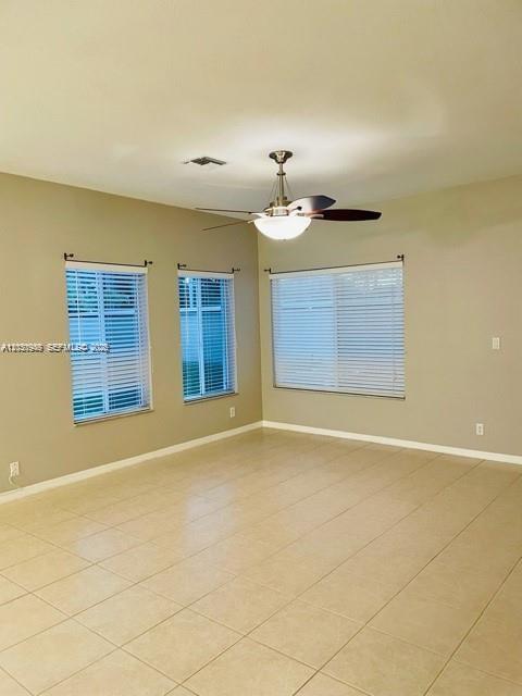 An empty room features beige tile flooring, a ceiling fan, and three windows with blinds — DEERFIELD BEACH, FL