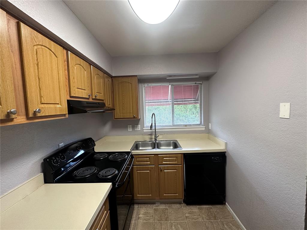 A kitchen features wood cabinets, a black stove, a double sink, and beige countertops — 4111 S SEMORAN BOULEVARD UNIT 3, ORLANDO, FL