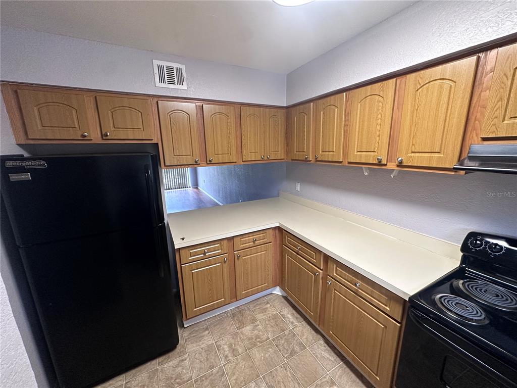 A kitchen features oak cabinets, black appliances, light countertops, and tiled flooring — 4111 S SEMORAN BOULEVARD UNIT 3, ORLANDO, FL