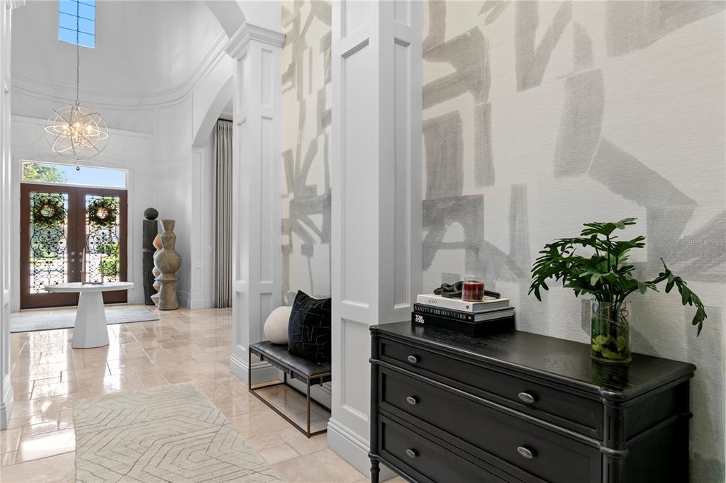 A bright, high-ceilinged foyer features a black chest, a bench, and patterned wallpaper — 15306 FISHHAWK PRESERVE DRIVE, LITHIA, FL