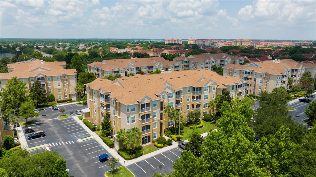 An aerial view shows multi-story apartment buildings with tan facades and brown shingled roofs — 2813 ALMATON LOOP UNIT 301, KISSIMMEE, FL