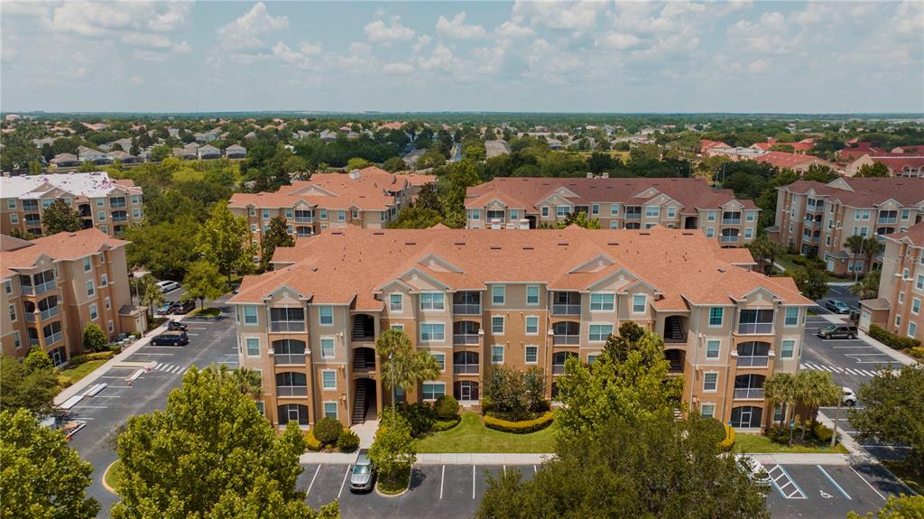 An aerial view shows a multi-story apartment complex with tan stucco walls and shingled roofs — 2813 ALMATON LOOP UNIT 301, KISSIMMEE, FL