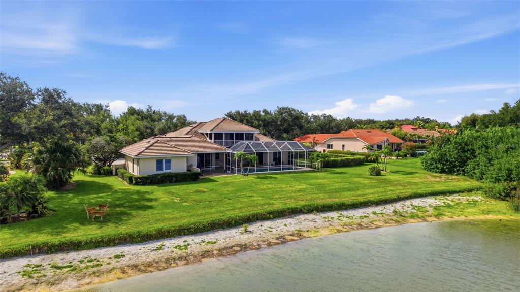 An aerial view of a house with a pool cage and lawn near a lake — 7389 S SERENOA DRIVE, SARASOTA, FL