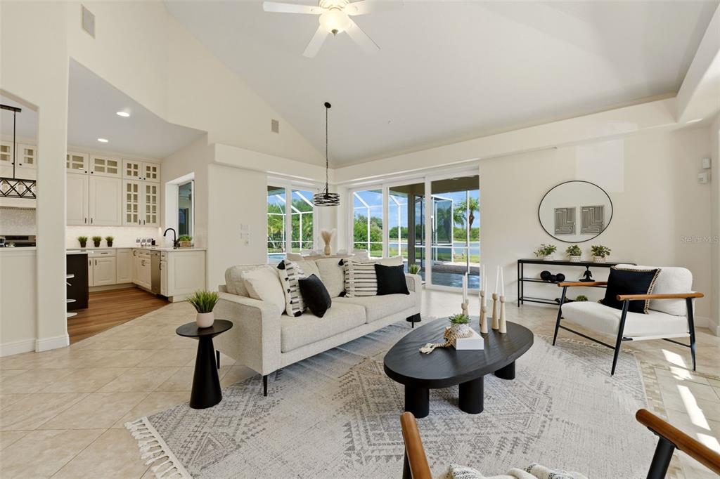A bright, open-concept living room features a vaulted ceiling, neutral tile floors, and sliding glass doors — 7389 S SERENOA DRIVE, SARASOTA, FL