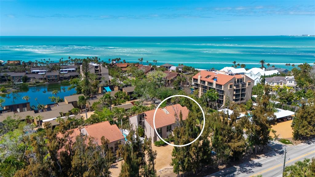 An aerial view shows a multi-story residential building with a tiled roof near the ocean — 115 PASS KEY ROAD UNIT 115, SARASOTA, FL