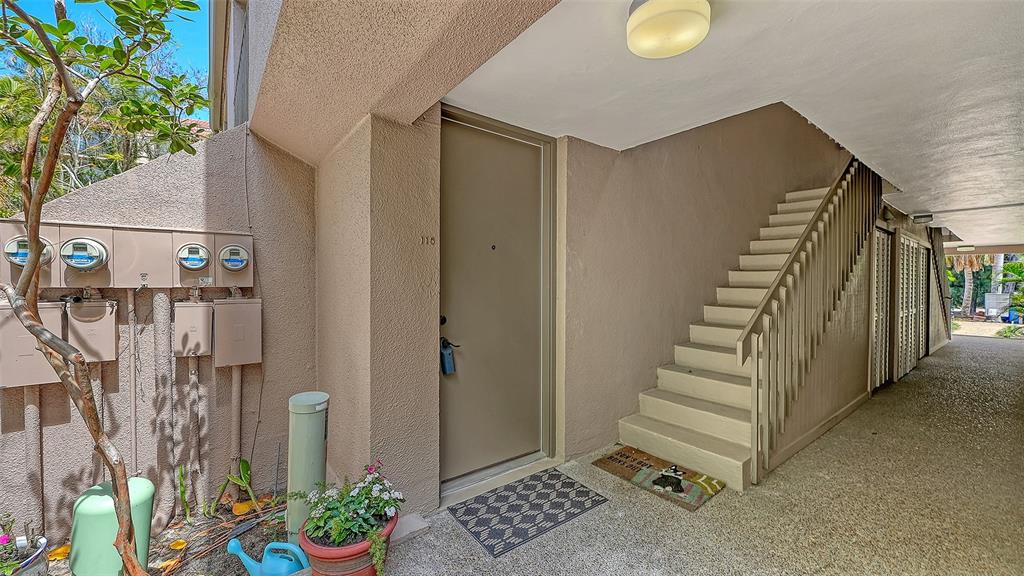 An exterior view of a ground-floor apartment entrance with a staircase and utility meters — 115 PASS KEY ROAD UNIT 115, SARASOTA, FL