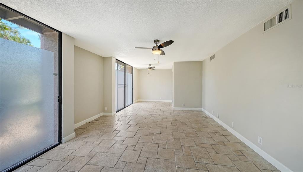 An empty room features beige tiled floors, two ceiling fans, and large sliding glass doors — 115 PASS KEY ROAD UNIT 115, SARASOTA, FL