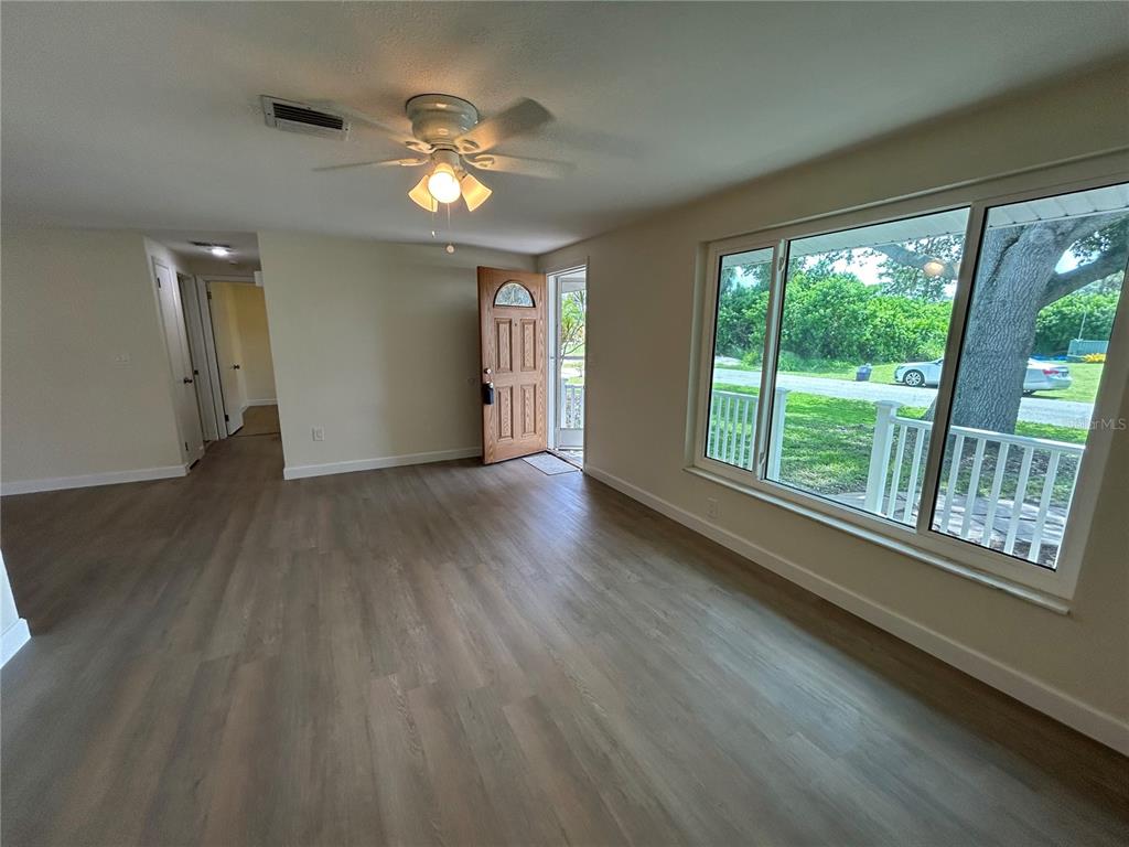 An interior view of a living room with wood-look flooring, a ceiling fan, and windows — 4485 COSTELLO STREET, PORT CHARLOTTE, FL