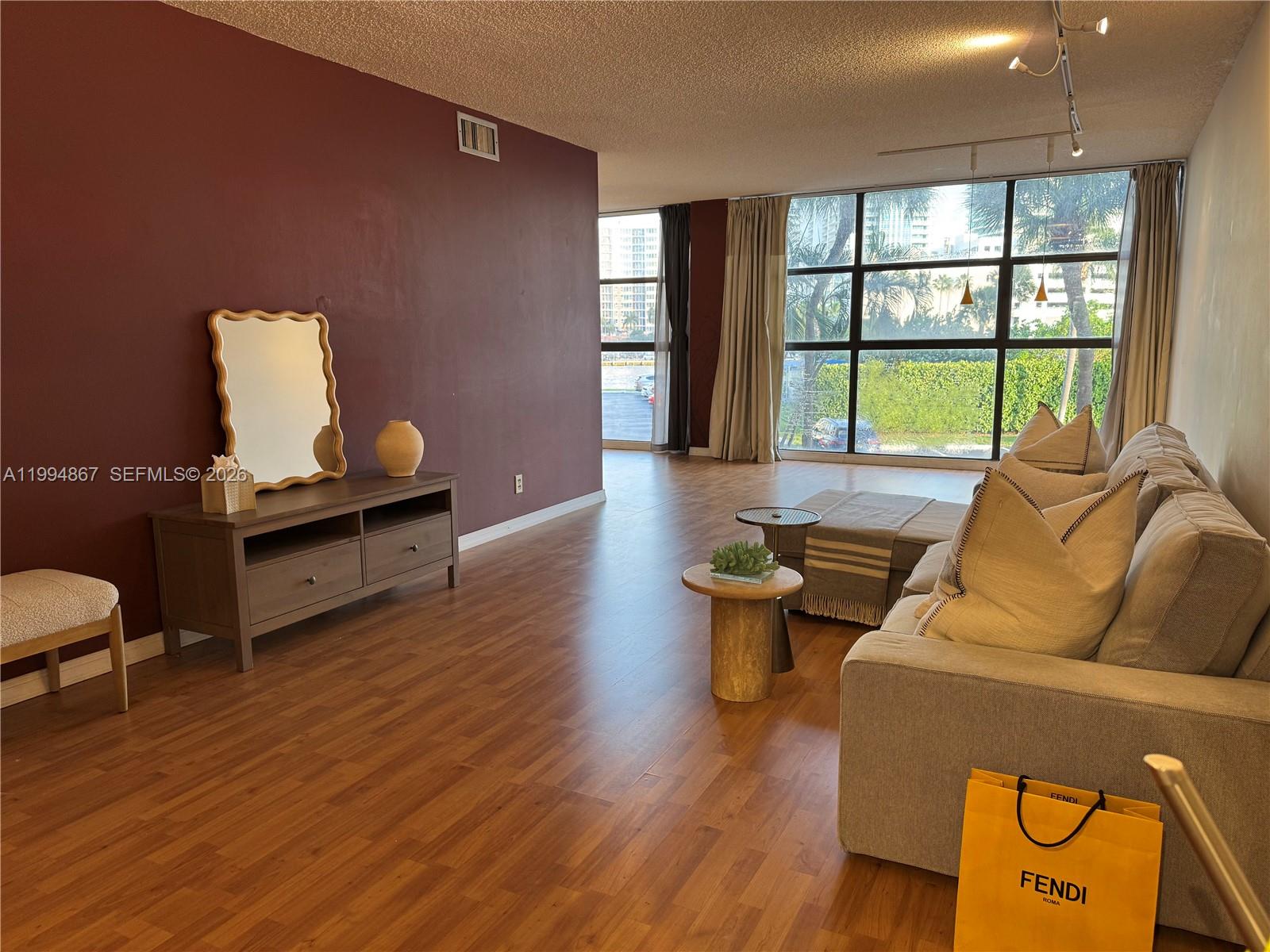 A living room features wood-look flooring, a dark accent wall, and floor-to-ceiling windows — 600 Parkview Dr # 222, Hallandale Beach FL 33009, HALLANDALE BEACH, FL