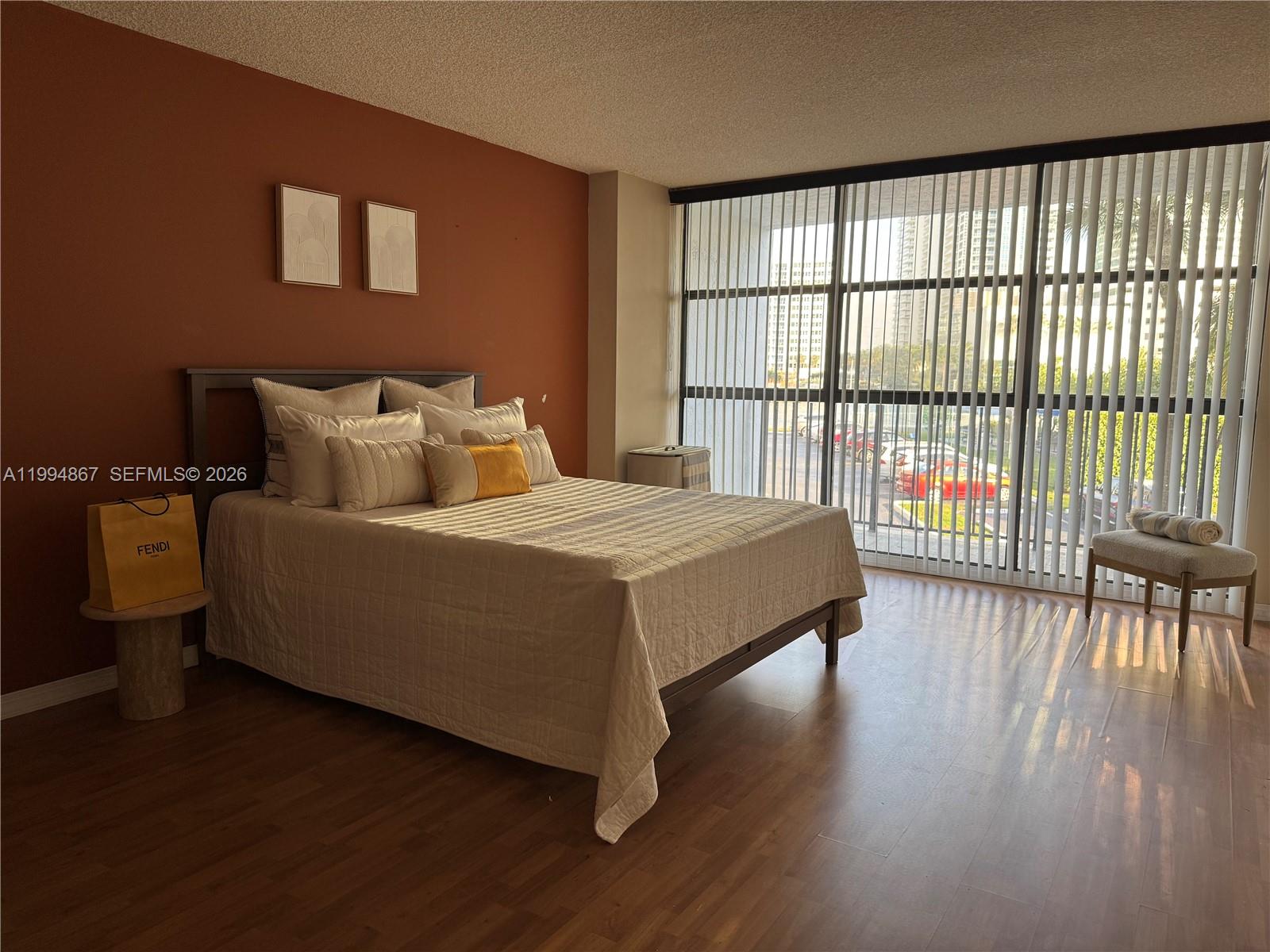A bedroom features a bed against a terracotta wall, wood flooring, and floor-to-ceiling windows — 600 Parkview Dr # 222, Hallandale Beach FL 33009, HALLANDALE BEACH, FL