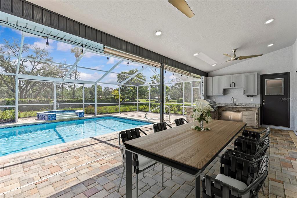 A covered patio features a dining table, outdoor kitchen, and a screened-in swimming pool — 9447 ASHLEY DRIVE, WEEKI WACHEE, FL