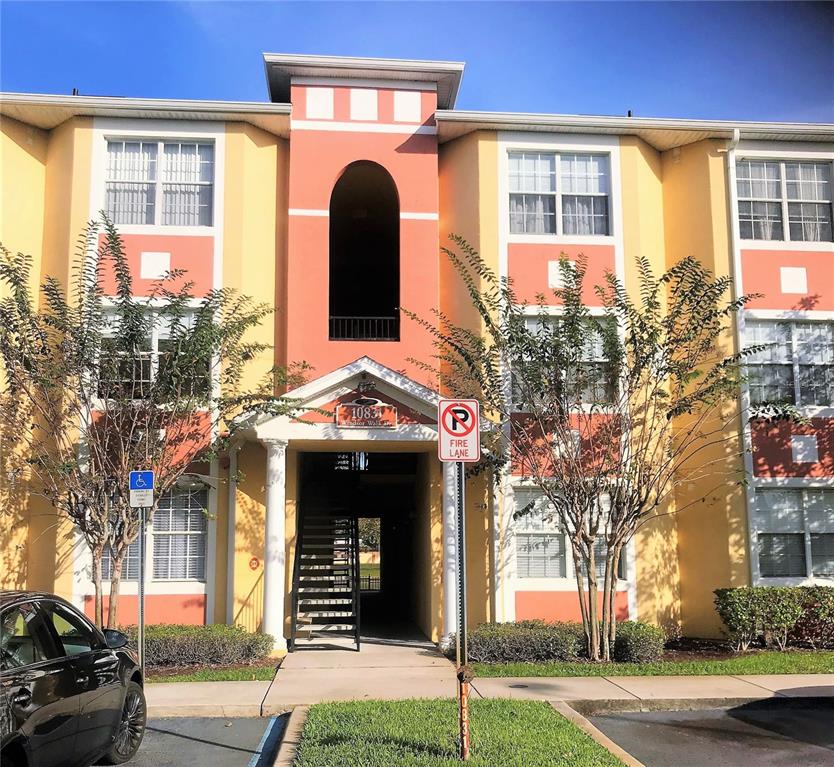 An exterior view of a three-story apartment building with yellow and peach-colored stucco walls — 10831 WINDSOR WALK DRIVE UNIT 1305, ORLANDO, FL