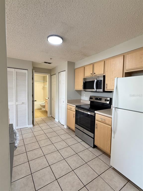 A kitchen with light wood cabinets, stainless steel appliances, and tile flooring — 10831 WINDSOR WALK DRIVE UNIT 1305, ORLANDO, FL