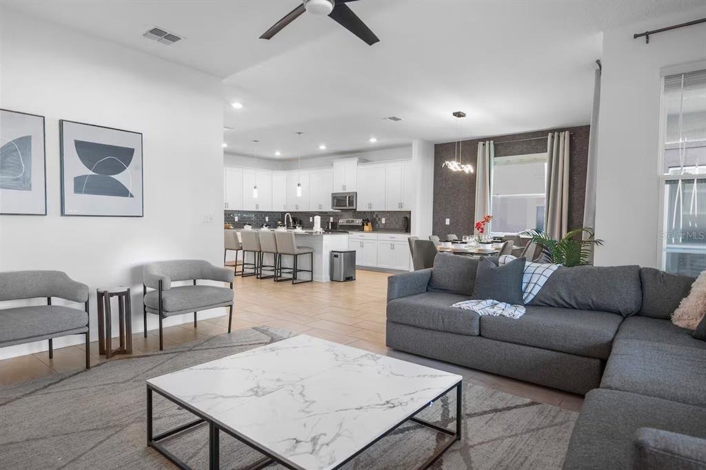 An open-concept living room features a gray sectional, marble coffee table, and a white kitchen — 1069 LEADER STREET, DAVENPORT, FL