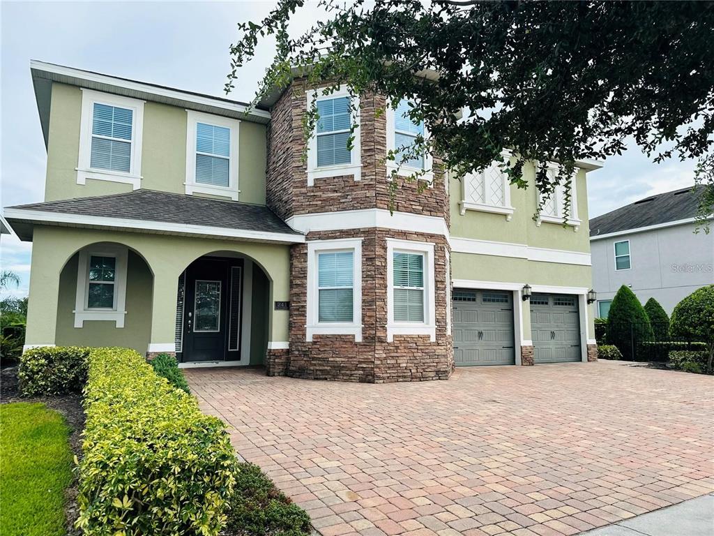 A two-story house with a stone facade, green stucco walls, and a paved driveway — 241 FALLS DRIVE, KISSIMMEE, FL