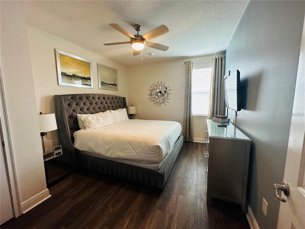 A bedroom features a tufted headboard, dark wood flooring, a ceiling fan, and a dresser — 241 FALLS DRIVE, KISSIMMEE, FL
